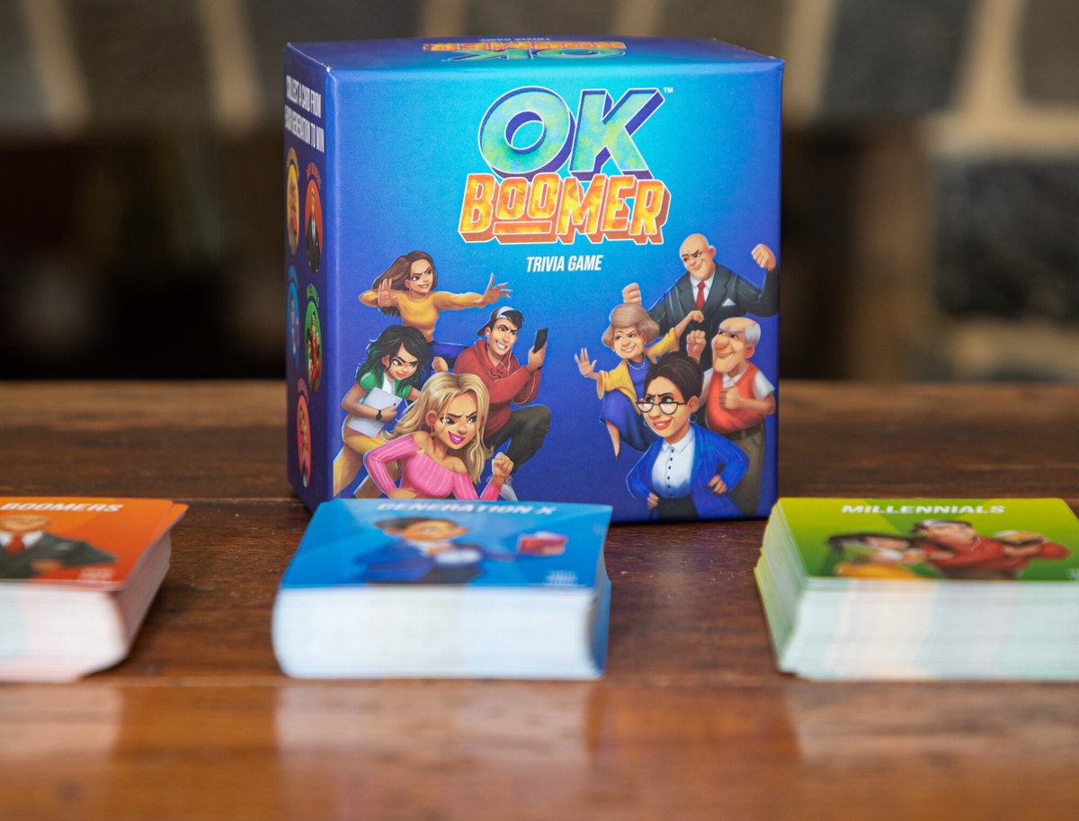 The OK Boomer trivia game box on a wooden table with generational card decks laid out in front